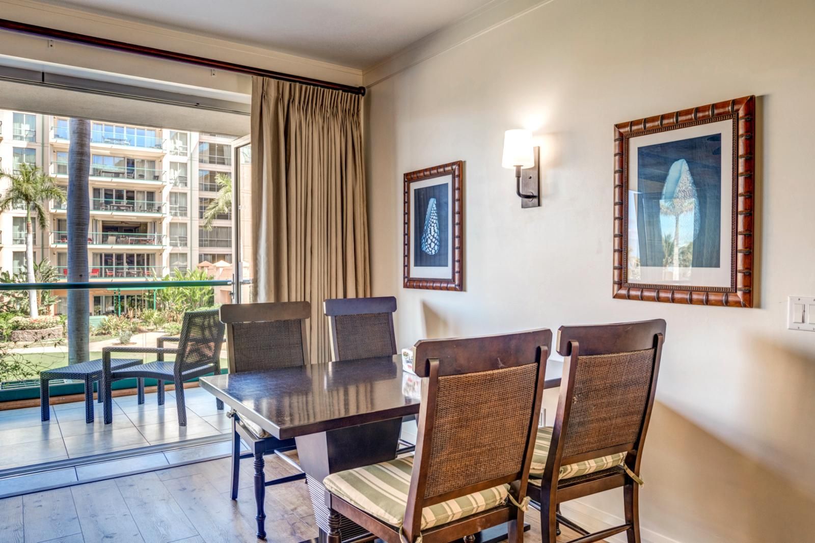 A hotel room with a dining table and chairs, a large window with curtains, and two framed pictures on the wall.