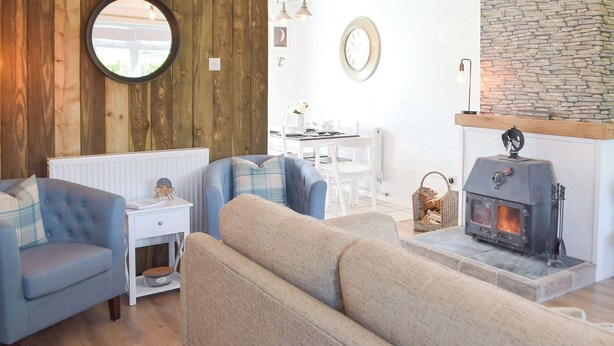 A cozy living room with a stone fireplace, a round mirror, and a dining area with white furniture. - The Captains Hideaway (Sageston, near Tenby)