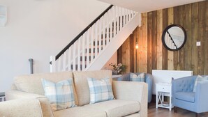A living room with a beige sofa, a blue armchair, a white coffee table, a wooden staircase, and a round mirror on the wall. - The Captains Hideaway (Sageston, near Tenby)