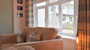 A cozy living room with a sofa, a small table, and a window with a sailboat model. - The Captains Hideaway (Sageston, near Tenby)