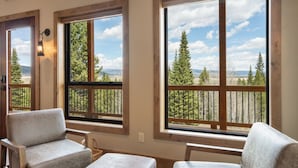 Ein Zimmer mit großen Fenstern und Blick auf Bäume und Berge. Es gibt zwei Polstersessel und eine hölzerne Bank.