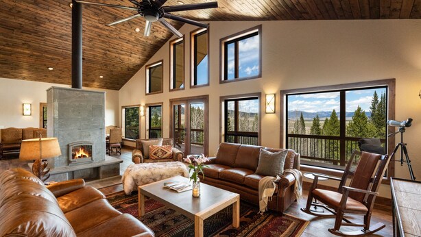 A spacious living room with a fireplace, leather sofas, a coffee table, and large windows offering mountain views.