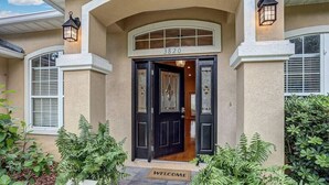 Une maison de couleur beige, avec une porte d’entrée noire, un paillasson et le numéro 3820 au-dessus de la porte.
