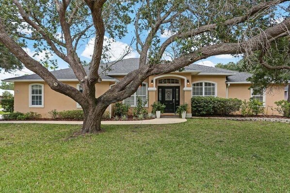 Une maison avec un grand arbre dans le jardin, une pelouse bien entretenue et une façade de couleur beige.