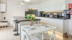 A modern kitchen with white cabinets, a central island, bar stools, and a dining table set for two.