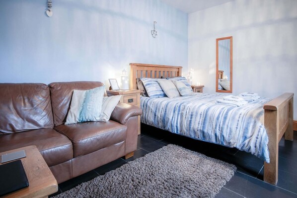 Ein Schlafzimmer mit einem braunen Ledersofa, einem Bett mit gestreifter Decke, einem Holznachttisch, einem Spiegel und einem kleinen Teppich.