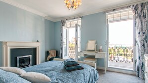 Una camera da letto con un letto, una cassettiera, una scrivania, una sedia, un camino e un balcone con vista.