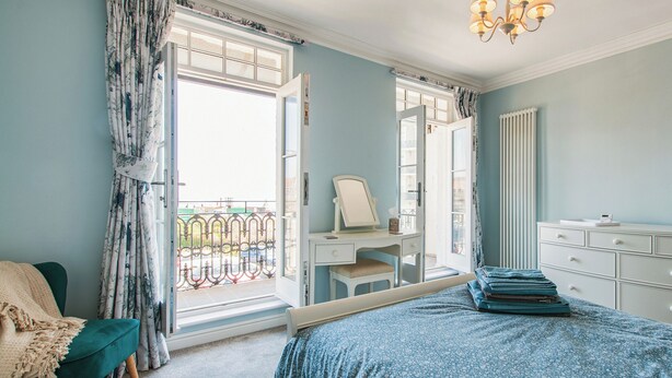 Una camera da letto con un letto, una scrivania, una sedia, un comò e un balcone con vista.