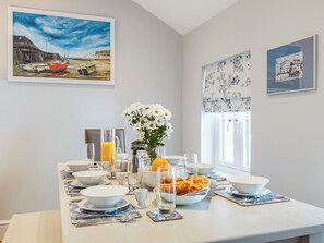 A dining table set with bowls, glasses, and a vase of flowers, with artwork on the walls.