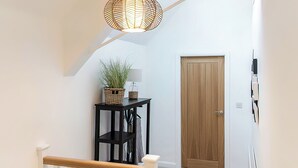Een trap met een houten leuning, een zwart metalen bijzettafeltje met een plant, een lamp en een houten deur.