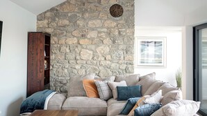 Een moderne woonkamer met een stenen muur, een houten kast, een beige bank met meerdere kussens en een houten salontafel.