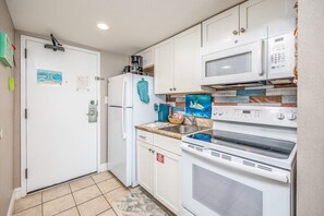 A compact kitchen with white cabinets, a microwave, a stove, and a refrigerator.