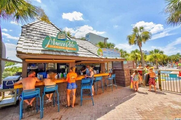 A beachside bar named Marco Polo with outdoor seating and a view of the pool area.