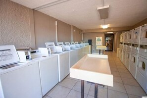 A laundry facility with multiple washing machines and dryers, a control panel, and a clear path leading to a door.