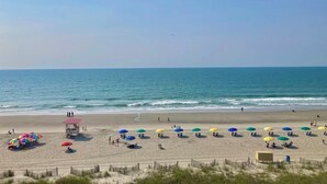 Une plage avec des parasols et des chaises longues, une tour de surveillance pour les sauveteurs, et l’océan.