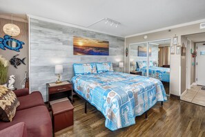 A bedroom with a large bed, a nightstand, a dresser, and a seating area with a sofa and ottoman.