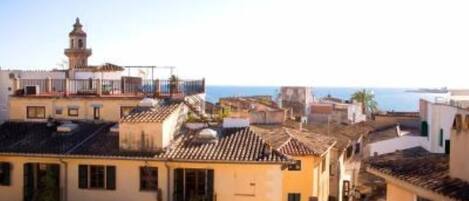 Uma cidade costeira com edifícios de telhados em terracota, uma torre imponente e vista para o mar.