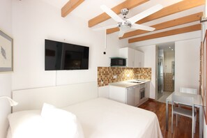 Een slaapkamer met een bed, een aan de muur bevestigde televisie, een kitchenette met een magnetron en een plafondventilator.