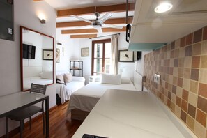 Une chambre d’hôtel avec deux lits, un bureau, une chaise, un ventilateur de plafond et une fenêtre avec des rideaux.