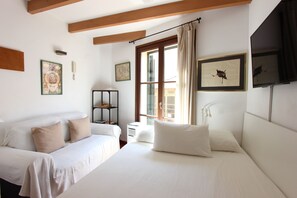 Une chambre à coucher avec un lit, un canapé, une fenêtre avec des rideaux et des œuvres d’art accrochées aux murs.