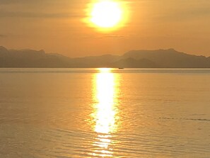 Auringonlasku tyynen vesistön yllä, taustalla kaukana kohoavat vuoret.