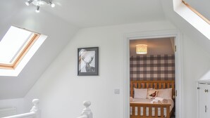 A bedroom with a sloped ceiling, a skylight, a framed picture, a bed with a checkered headboard, and a bedside lamp.