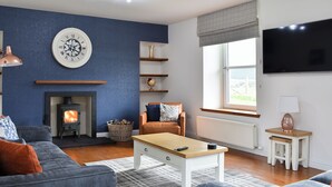 A living room with a fireplace, a clock, a television, and a window with a view.