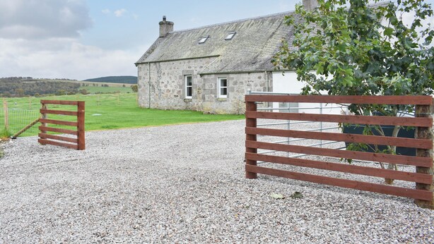 A stone house with a gravel driveway and a wooden gate.