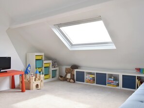 Une salle de jeux pour enfants avec un plafond en pente, un château jouet, des meubles de rangement et un téléviseur.