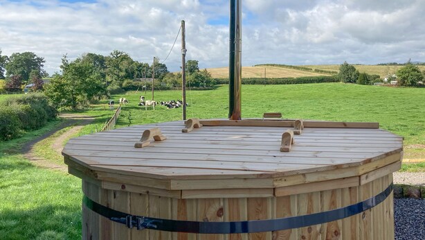 A wooden hot tub with a view of a grassy field and cows in the background.