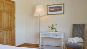 A bedroom with a bed, a bedside table with a lamp, a chair, and a framed picture on the wall.