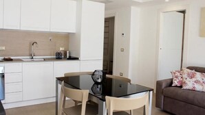 Una cocina moderna con armarios blancos, encimera negra y una mesa de comedor de vidrio con dos sillas.