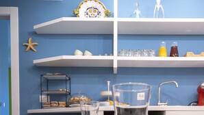 Una cocina con armarios blancos, una pared azul y una estantería con adornos.