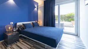 Un dormitorio moderno con una cama grande, una mesita de noche con lámpara y vistas al exterior a través de un ventanal corredero.