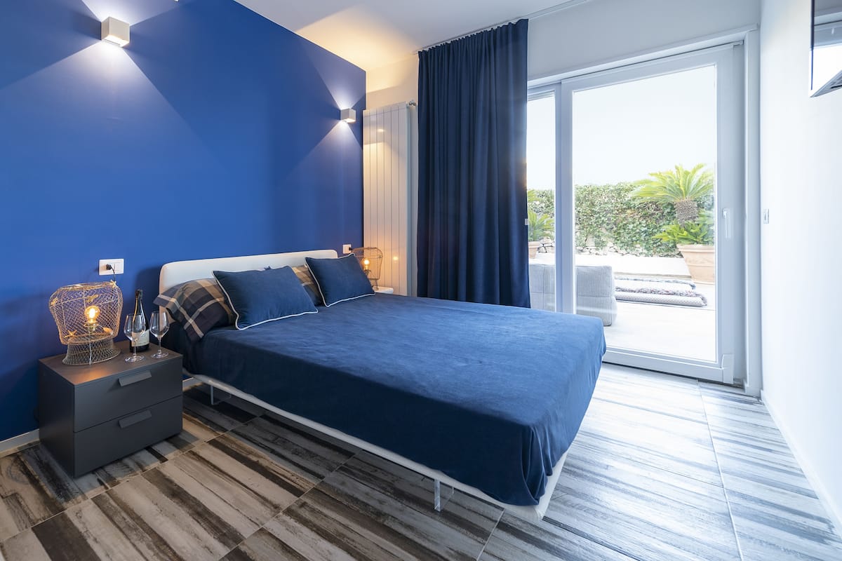 Un dormitorio moderno con una cama grande, una mesita de noche con lámpara y vistas al exterior a través de un ventanal corredero.
