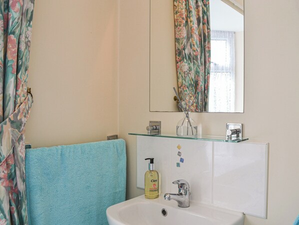 A bathroom with a white sink, a mirror, a glass cabinet, and a blue towel.