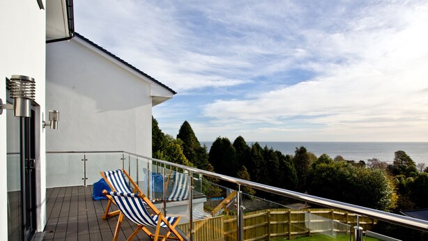 A balcony with two striped lounge chairs, a glass railing, and a view of the sea.