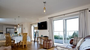 A modern living room with a leather sofa, dining area, and a large window with curtains.