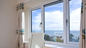 A room with a wooden desk, a framed picture, and a view of the sea through a window.