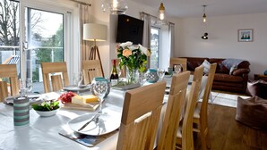 A dining area with a table set for four, chairs, a vase with flowers, and a sofa in the background.