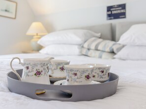 A tray with teacups and a teapot on a bed with pillows and a sign in the background.