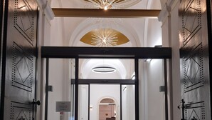 Une entrée d’hôtel moderne avec une porte en verre, un plafond doré et une enseigne indiquant « The Gold Bank ».