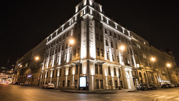 Un grand bâtiment historique, doté de plusieurs étages et d’une entrée d’angle remarquable, illuminée par des lampadaires.