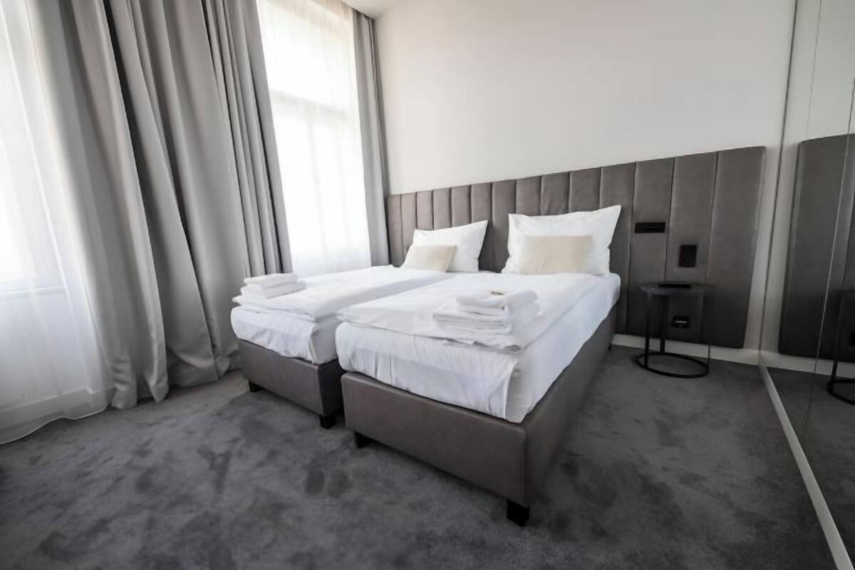 Habitación de hotel con cama doble, dos mesitas de noche, cabecero y un ventanal con cortinas.