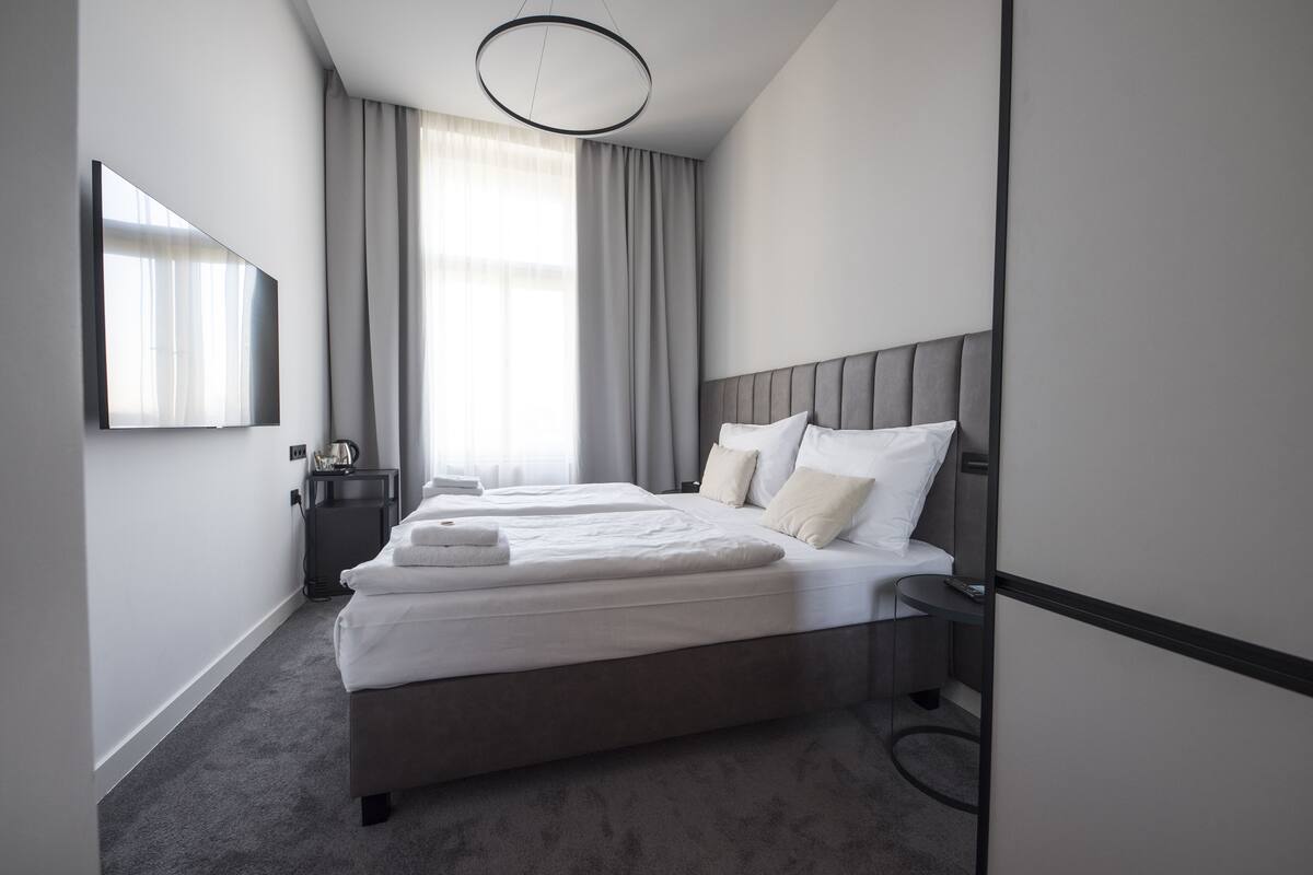Una habitación de hotel moderna con una cama grande, una mesita de noche, un televisor de pantalla plana y una ventana con cortinas.