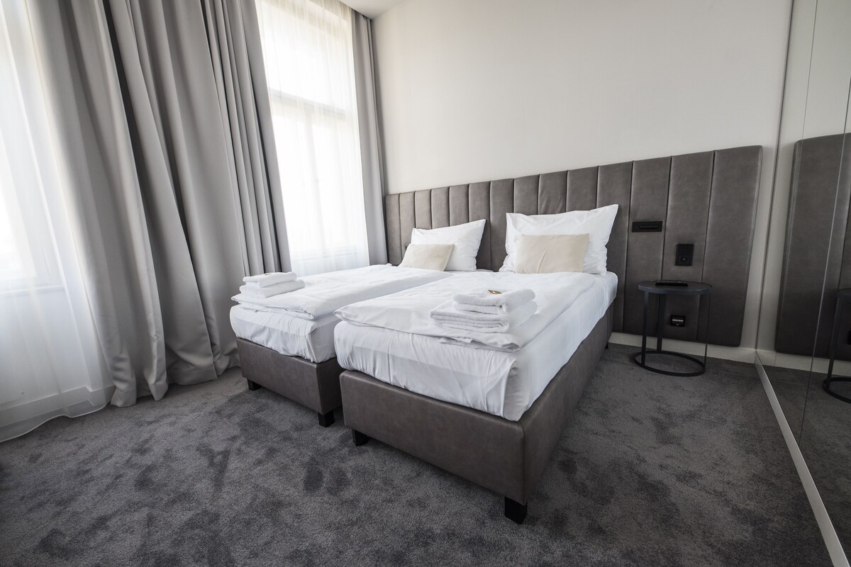 Una habitación de hotel moderna con una cama grande, una mesita de noche y un ventanal con cortinas.