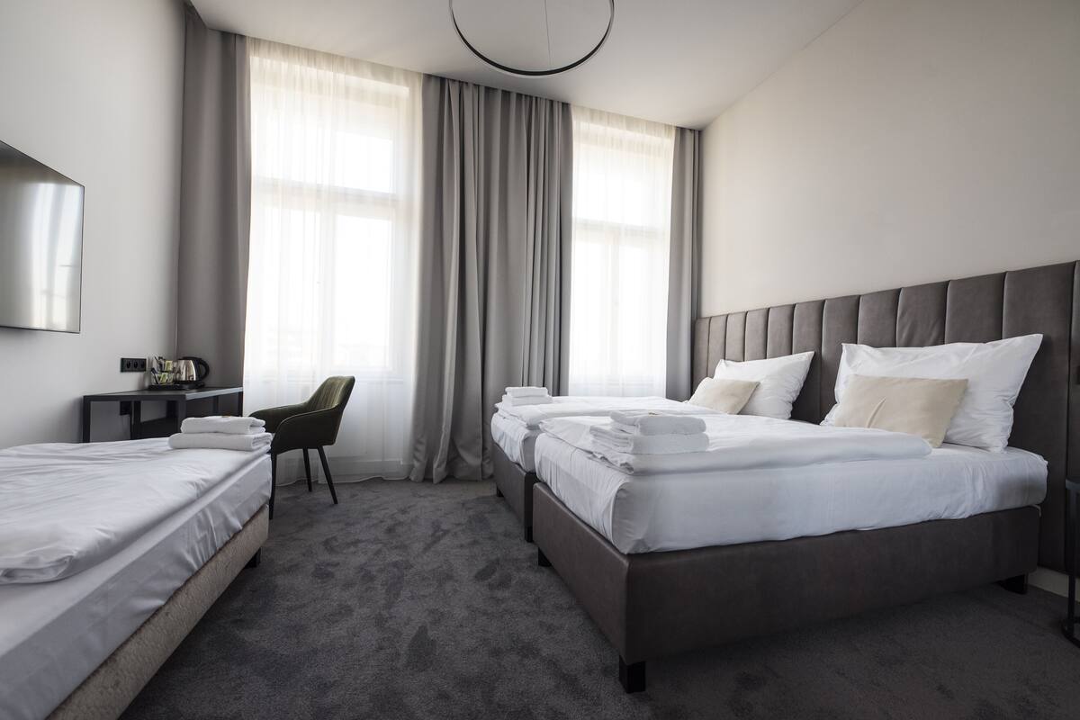 Habitación de hotel con dos camas, un escritorio con silla, un televisor de pantalla plana y un ventanal con cortinas.