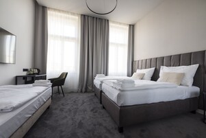 Quarto de hotel com duas camas, uma escrivaninha com cadeira, televisão de tela plana e uma janela grande com cortinas.