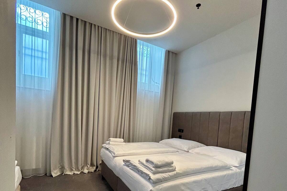 Habitación de hotel moderna con una cama grande, una lámpara de techo redonda y vistas al exterior a través de una ventana con cortinas.