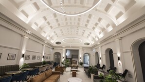Un hall d’entrée spacieux avec un plafond haut, des coins salon et un escalier central.